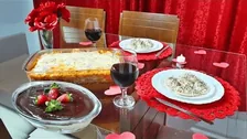 Mesa com pratos, travessa gratinada e taças de vinho, no depoimento de Juliana S.