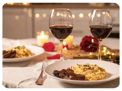 Mesa de jantar a dois com risoto, carne, taças de vinho e velas