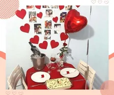 Mesa para dois decorada com corações vermelhos, fotos e pratos de jantar, no depoimento de Ana M.